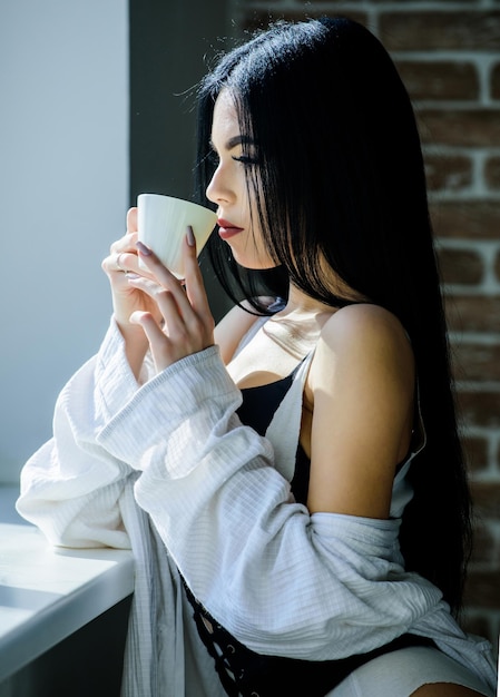 Amante misterioso apaixonado Hora do café perfeito Mas primeiro café Aproveitando a luz do sol da manhã Garota sensual seios sensuais tomando café perto do parapeito da janela Lingerie feminina atraente relaxando em casa