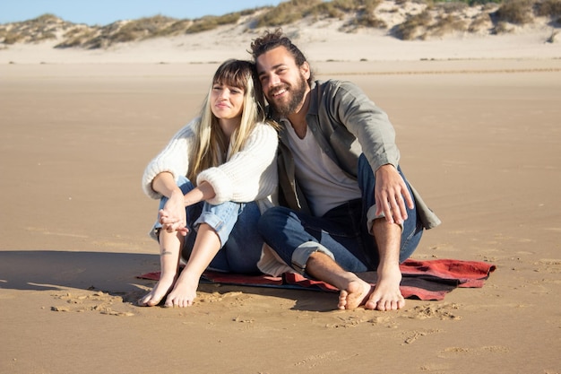 Amante pareja caucásica en vacaciones de verano. Hombre y mujer barbudos con ropa informal sentados en una manta, apoyados en el hombro. Amor, viajes, concepto de ternura.