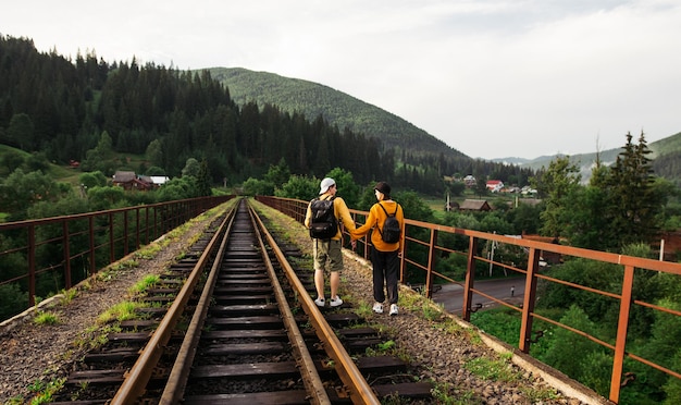 Amante pareja de turistas en ropa casual caminando tomados de la mano en el puente ferroviario