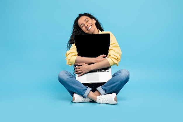 Amante de la tecnología mujer emocionada abrazando la computadora portátil en el estudio