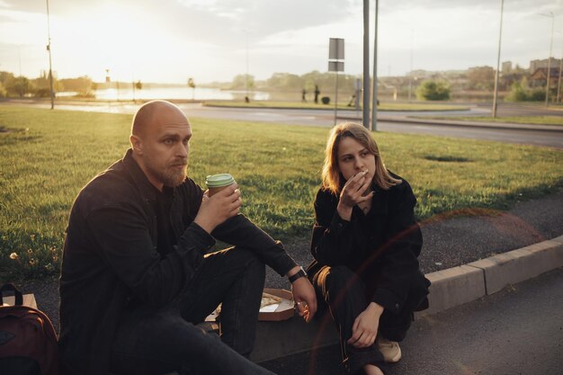 Los amantes comen pizza sentados en el césped durante la puesta de sol