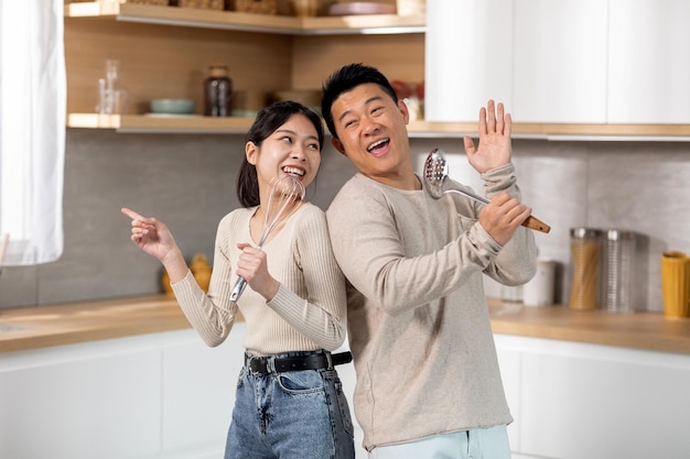 Amantes cônjuges asiáticos cantando enquanto cozinham juntos