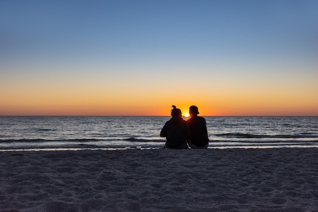 Amantes da praia assistindo o pôr do sol sentado em uma praia de areia