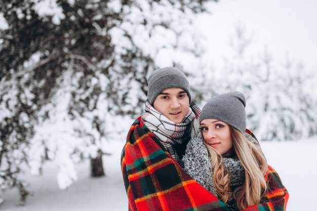 Los amantes están cubiertos con una manta con el telón de fondo de un bosque nevado de invierno