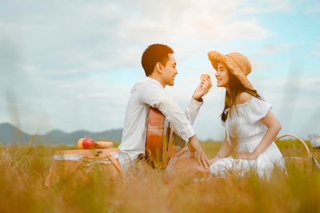 Amantes felices sentados en la pradera mirándose con ternura. Los hombres tienen guitarras y dan manzanas a las mujeres. Se miran con amor y sonrisas.