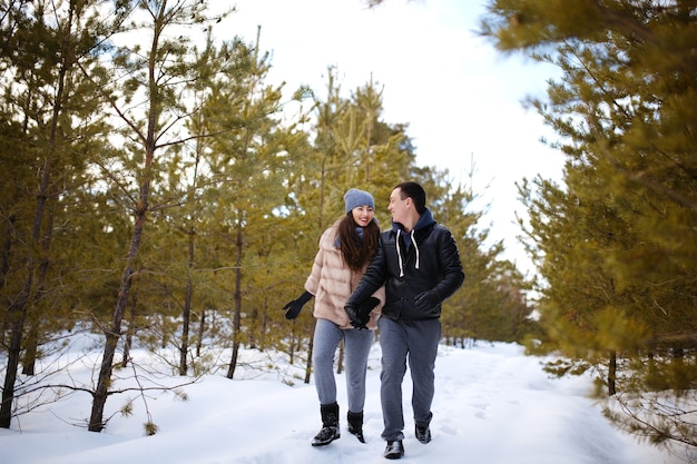 Amantes felices tomados de la mano caminan en el bosque de abetos en la nieve