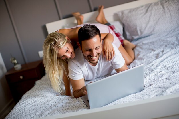 Amantes íntimos usando la computadora portátil acostada en la cama en el dormitorio