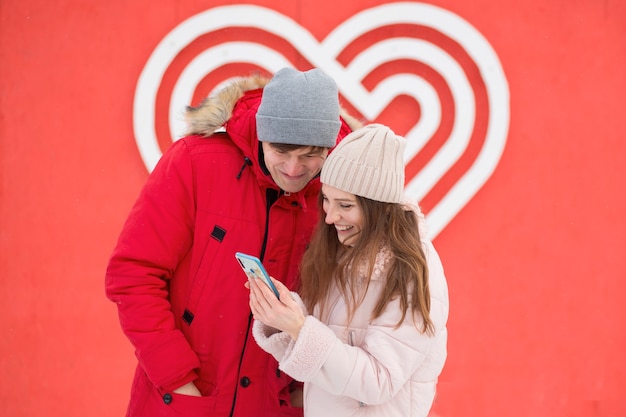 Amantes jóvenes con teléfono cerca de gran corazón. Día de San Valentín