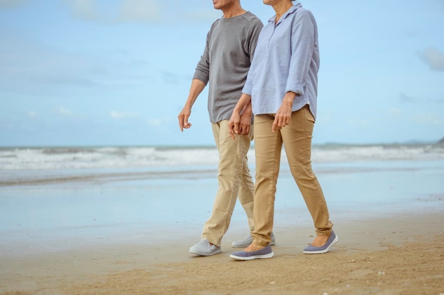 Los amantes mayores caminan de la mano en la playa al amanecer, planifican un seguro de vida en el concepto de jubilación.