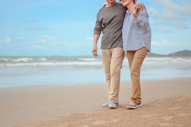 Los amantes mayores caminan de la mano en la playa al amanecer, planifican un seguro de vida en el concepto de jubilación.