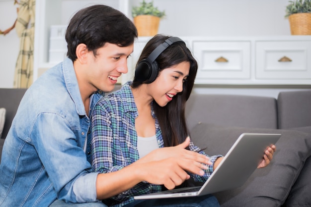 Amantes o pareja usando laptop y escuchando música con auriculares en casa