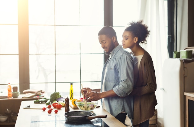 Amantes de la pareja negra haciendo ensalada. Familia feliz cocinar comida vegetariana en cocina tipo loft