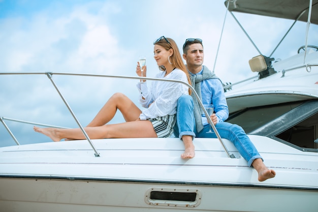 Amantes que passam o tempo feliz em um iate no mar. Honeymood de luxo em um barco marítimo. Conceito de férias, viagens, mar, amizade e pessoas. Casal sorridente, sentado e conversando no convés do iate