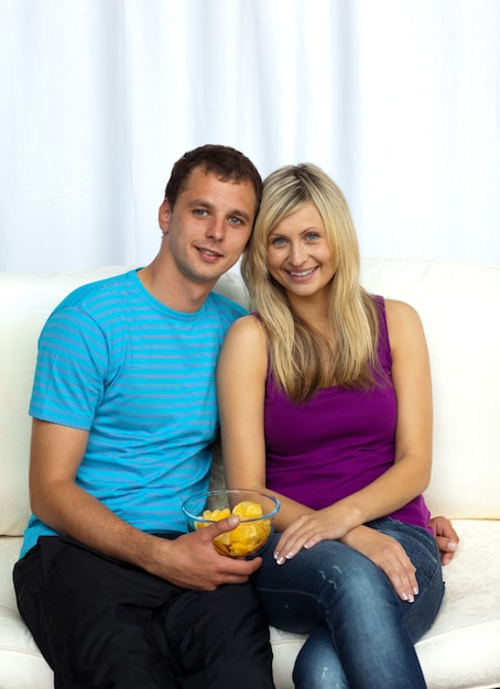 Amantes sonrientes viendo la televisión y comiendo patatas fritas