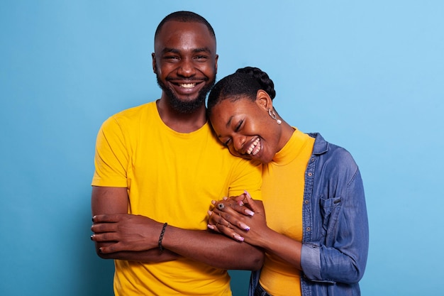 Amantes sorridentes de mãos dadas e ligação no estúdio, mostrando carinho com abraço romântico. Pessoas positivas apaixonadas expressando gratidão, abraçando juntos sobre fundo azul.