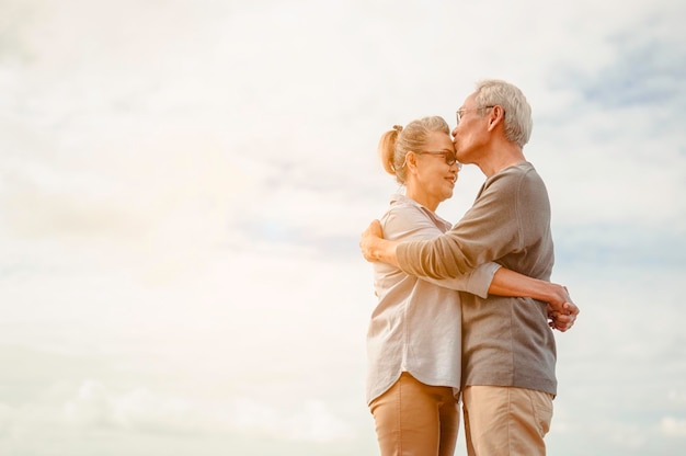 Los amantes de la tercera edad se abrazan y se besan en la puesta de sol en la playa Planifique un seguro de vida con un concepto de jubilación feliz.