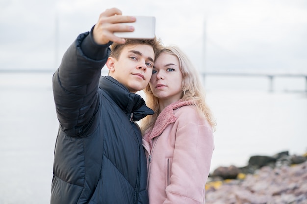 Amar a los adolescentes en la cita. Lindo chico morena y hermosa chica rubia toman selfie en teléfono celular