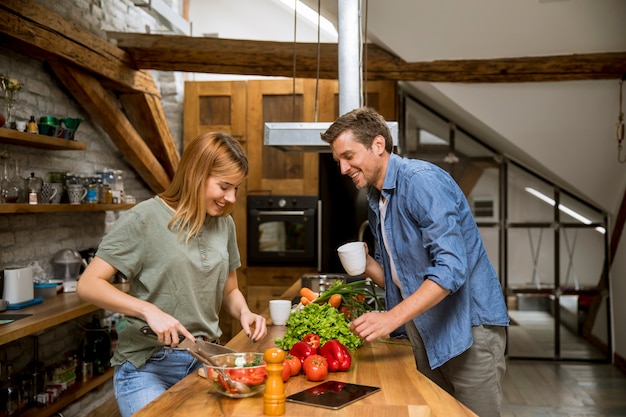 Amar o jovem casal cortar legumes juntos na cozinha rústica