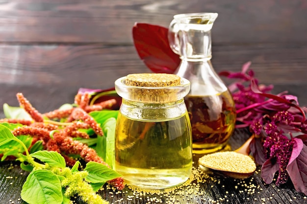 Amaranth-Öl in einem Glasgefäß und Dekanter-Amaranth-Samen in einem Löffel braun-grüne und violette Blumen und Pflanzenblätter auf einem Holzbrett-Hintergrund