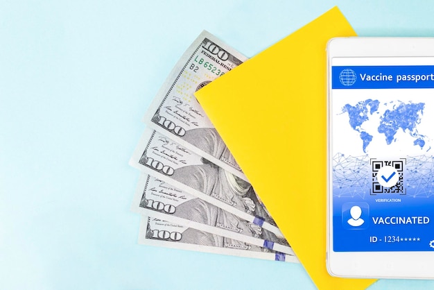 Amarelo um pedaço de papel dólares americanos e certificado digital COVID em uma tela de smartphone em fundo azul