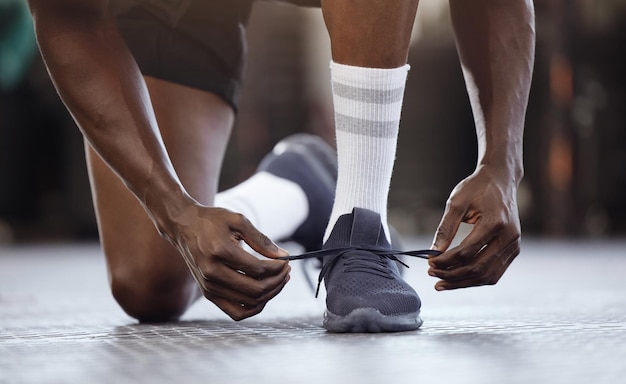 Amarre a aptidão e as mãos nos sapatos na academia para treinamento ou exercício ou corredor pronto para começar a se exercitar Objetivos do homem negro e amarre tênis de corrida na prática ou aula de saúde de desempenho esportivo