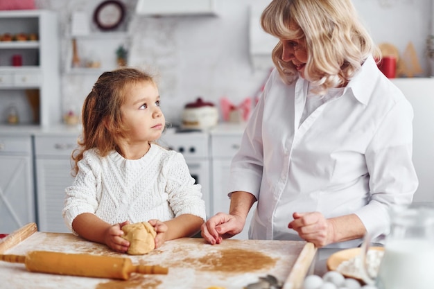 Amasa la masa La abuela mayor con su nieta cocina dulces para Navidad en la cocina