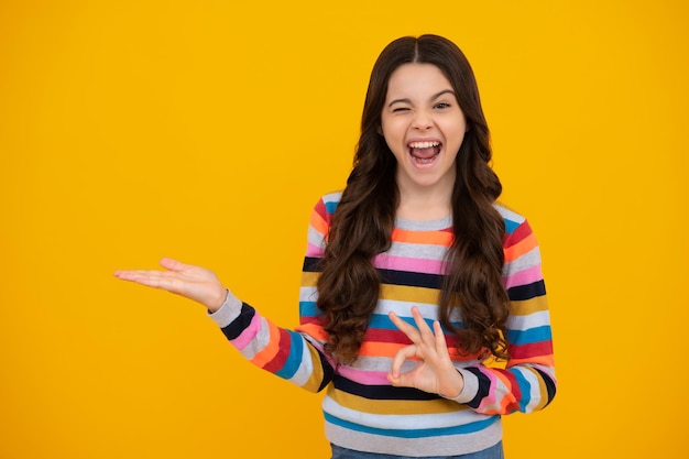 Amazed Teenager Porträt von niedlichen Teenager-Kind-Mädchen, das mit der Hand zeigt, die Anzeigen mit Kopierraum auf gelbem Hintergrund zeigt Aufgeregtes Teenager-Mädchen