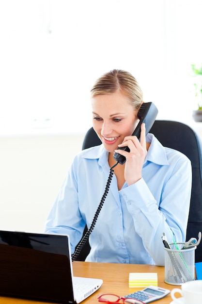 Ambiciosa mujer de negocios hablando por teléfono con su computadora portátil