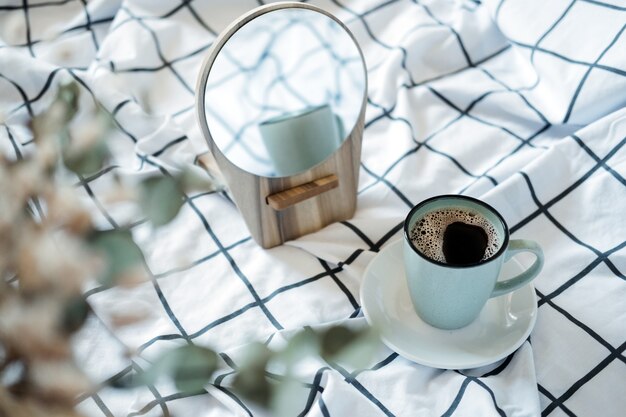 Ambiente acogedor por la mañana. Café en la cama. Una taza de café negro en la cama sobre una manta a cuadros blanca. Enfoque selectivo