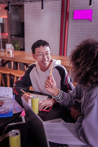 Ambiente amistoso. Alegre colegial asiático manteniendo una sonrisa en su rostro mientras está en todos los oídos