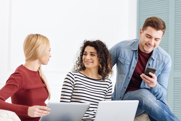 Ambiente amistoso. Mujeres alegres que se miran y mantienen sonrisas en los rostros mientras sostienen las computadoras portátiles en las rodillas