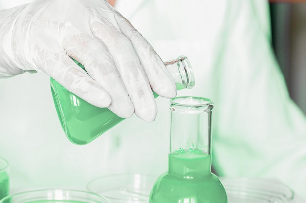 Ambiente de laboratório Assistente de laboratório realiza manipulações no laboratório Vestindo jaleco Tons verdes proeminentes Empregando instrumentos de vidro Focado na pesquisa de plantas no laboratório verde