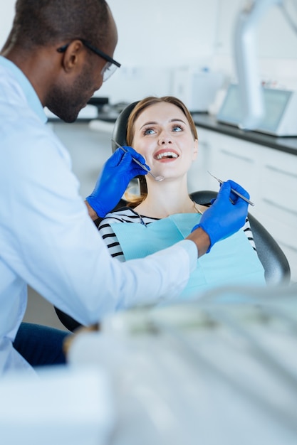 Ambiente positivo. paciente simpática, sorrindo para o dentista enquanto faz um exame completo dos dentes durante um check-up regular