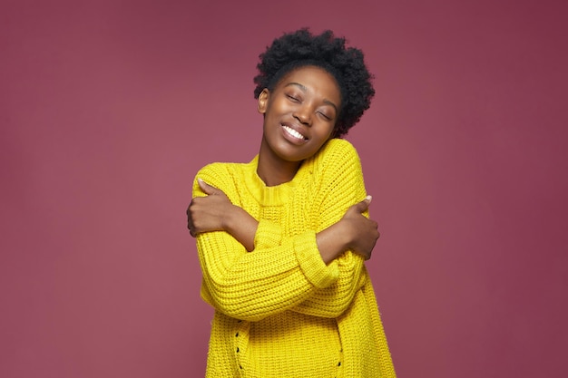 Ame-se, auto-aceitação, sorrindo, jovem afro-americana, abraça-se com os olhos fechados