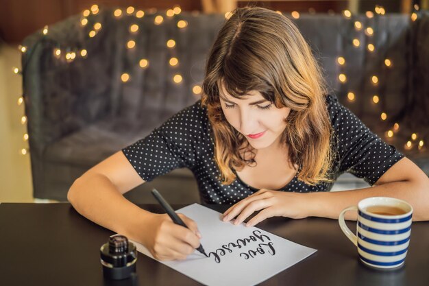 Ame-se calígrafa jovem escreve frase em papel branco Inscrevendo letras decoradas ornamentais Design gráfico de caligrafia letras conceito de criação de caligrafia