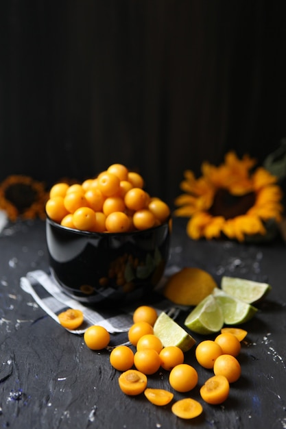 Ameixas amarelas com limão e lima no fundo preto. Ingredientes para uma geléia. Fotografia de alimentos. Imagem vertical. Girassol amarelo, conceito de outono, frutas saborosas e vitaminas.