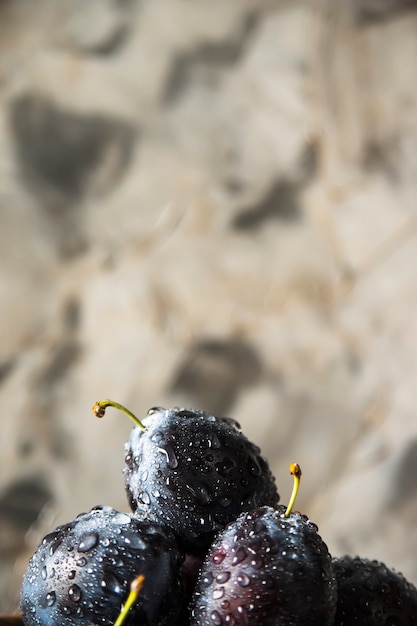 Ameixas azuis maduras com gotas da água em um fundo cinzento.