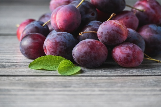 Ameixas colhidas na mesa de madeira frutas de ameixa roxa espaço de cópia de folha verde