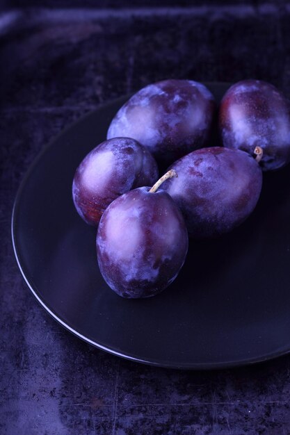 Ameixas frescas são roxas escuras, doces e cheias de suco Ameixas maduras e suculentas, cultivadas em casa, estão em uma placa preta sobre fundo escuro