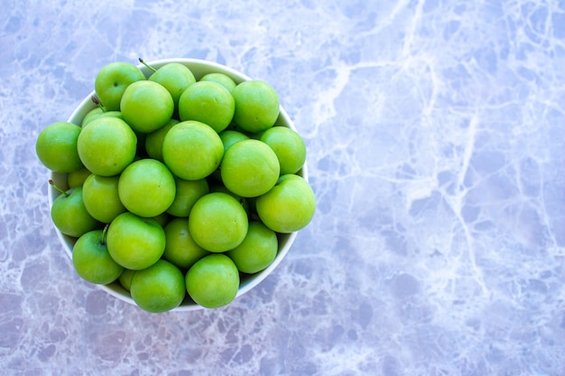 Ameixas verdes em uma tigela no fundo de mármore. Foto de vista superior de frutas de ameixa.