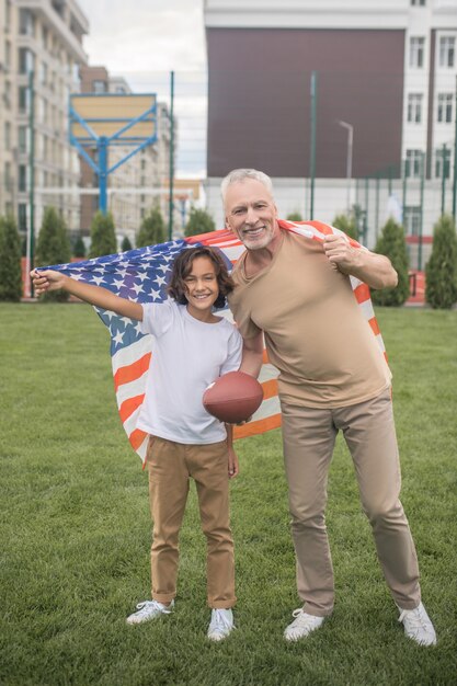 Amerikaner. Dunkelhaariger Junge in einem weißen T-Shirt und sein Vater mit einer Flagge