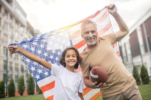 Amerikaner. Dunkelhaariger Junge in einem weißen T-Shirt und sein Vater mit einer Flagge