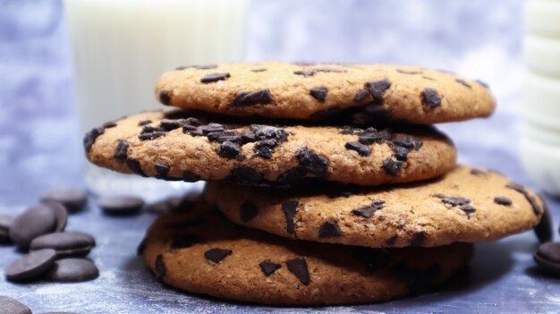 Amerikanische Chocolate Chip Cookies übereinander gestapelt mit Milch in einem Glas auf grauem Hintergrund. Traditioneller abgerundeter knuspriger Teig mit Schokoladenstückchen. Bäckerei. Leckeres Dessert, Gebäck.