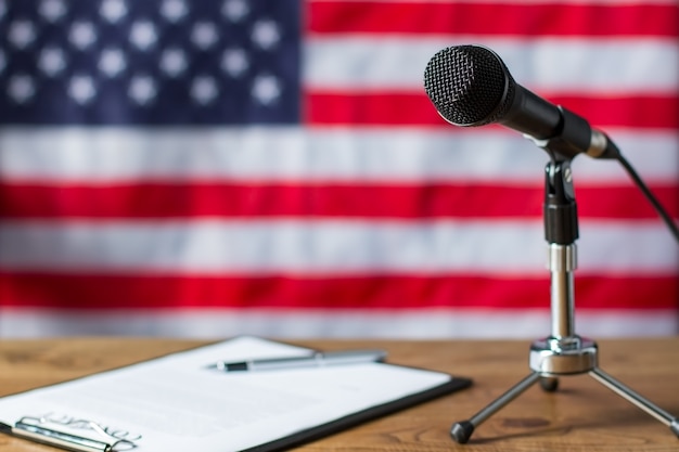 Amerikanische Flagge, Mikrofon und Papier. Zwischenablage und Mikrofon neben Banner. TV-Show-Szenario auf dem Tisch. Hinweise des Nachrichtenmoderators.