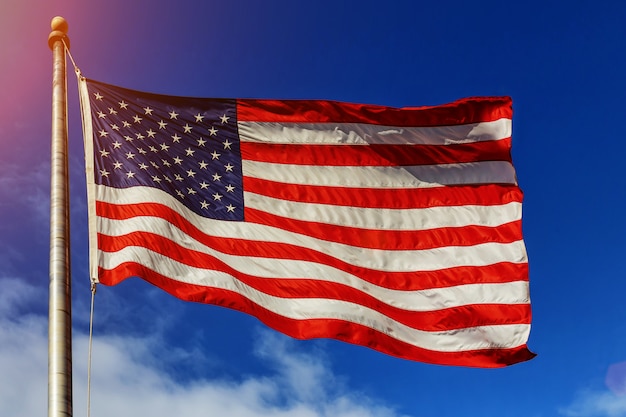 Amerikanische Flagge - Stern und Streifen, die über einen bewölkten blauen Himmel schwimmen