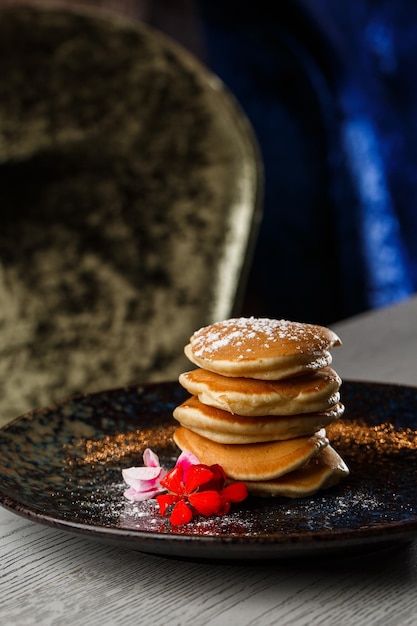 Amerikanische Pfannkuchen mit Beeren und Ahornsirup auf schwarzem Teller isoliert auf dunklem Hintergrund Café-Menü