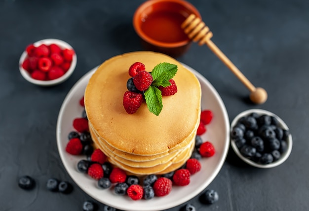 Amerikanische Pfannkuchen mit Himbeeren, frischen Blaubeeren und Honig. Gesundes Frühstück auf Beton