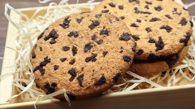 Amerikanische Schokoladenkekse auf einer braunen Holztischnahaufnahme in einer Schachtel. Traditioneller abgerundeter knuspriger Teig mit Schokoladenstückchen. Bäckerei. Leckeres Dessert, Gebäck. Ländliches Stillleben.