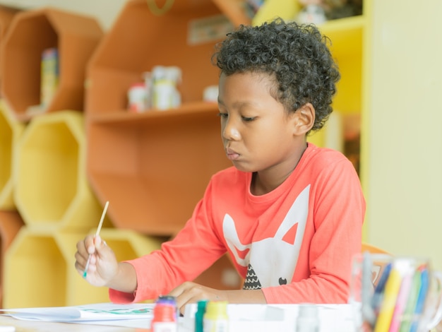 Amerikanischer Junge, der Haus trägt, trug Zeichnungsfarbbleistifte im Kindergartenklassenzimmer