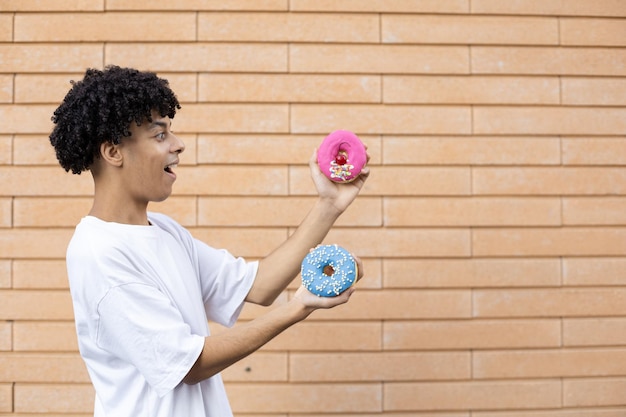 Amerikanischer Kerl, der seitlich steht und ein weißes T-Shirt trägt, das einen rosa und blauen Donut auf seiner Seite hält